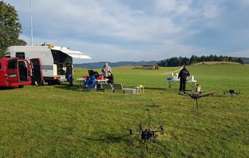 Forschungsteam mit Messfahrzeug und mehreren Drohnen auf einer Wiese im freien Gelände.