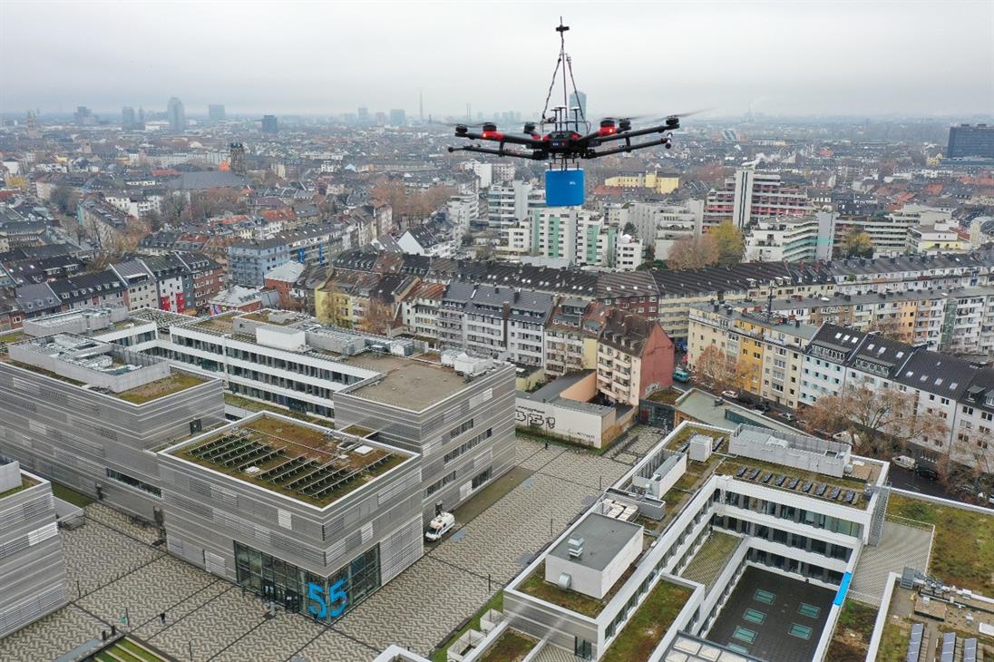 Drohne mit Messsensor über dem Hochschulgebäude der Hochschule Düsseldorf vor urbaner Stadtkulisse.